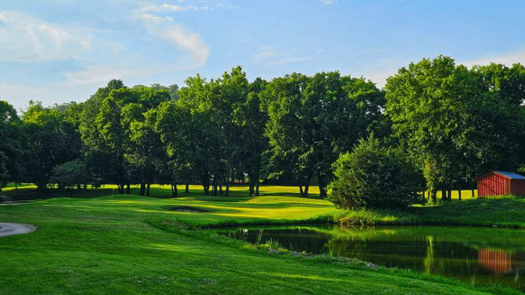 View of golf course with trees and pond