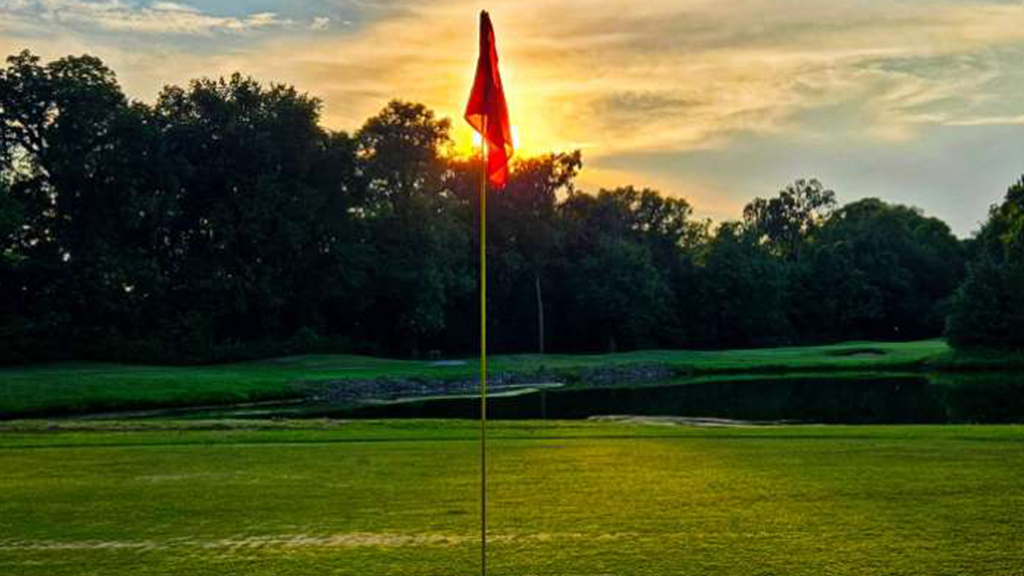Red flag over hole on golf course at sunset